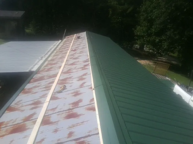 Old rusted panels beside newly installed green metal roofing — Wind Damage Roof Repair by Roofing Brothers in Osprey