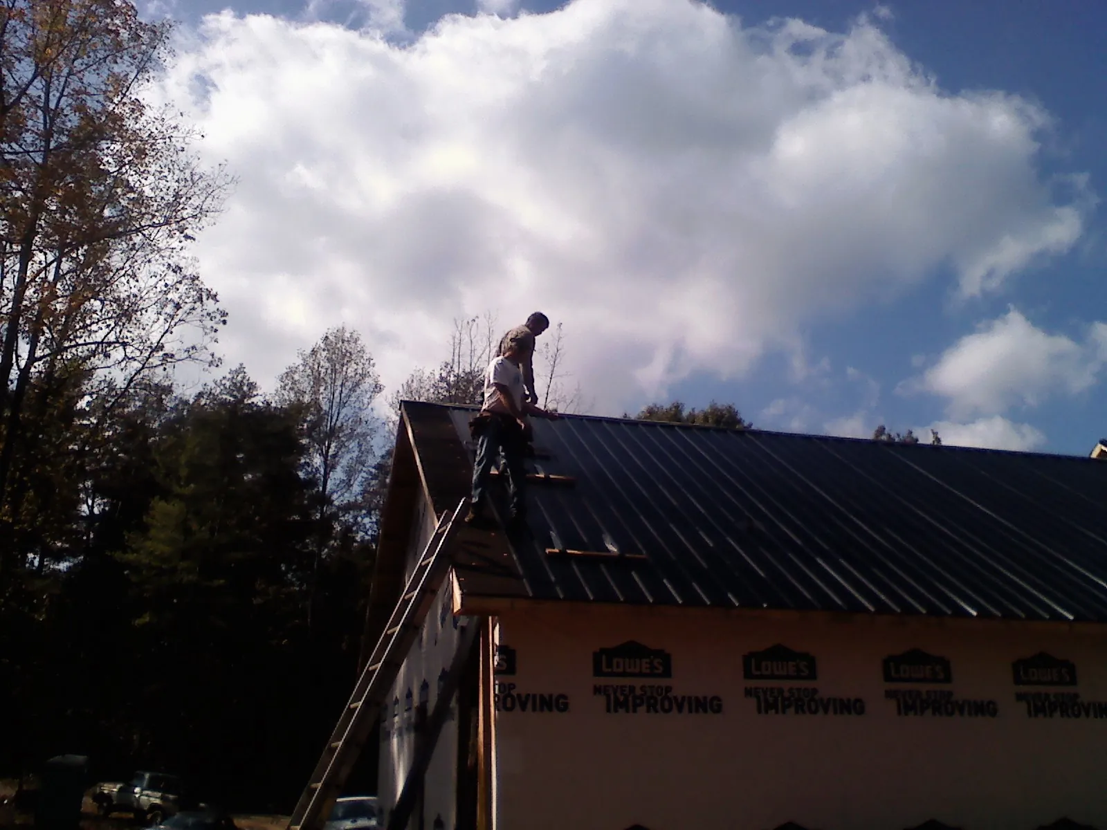 Roofer fastening dark metal panels high against a cloudy sky, from a Roof Inspection job in Osprey