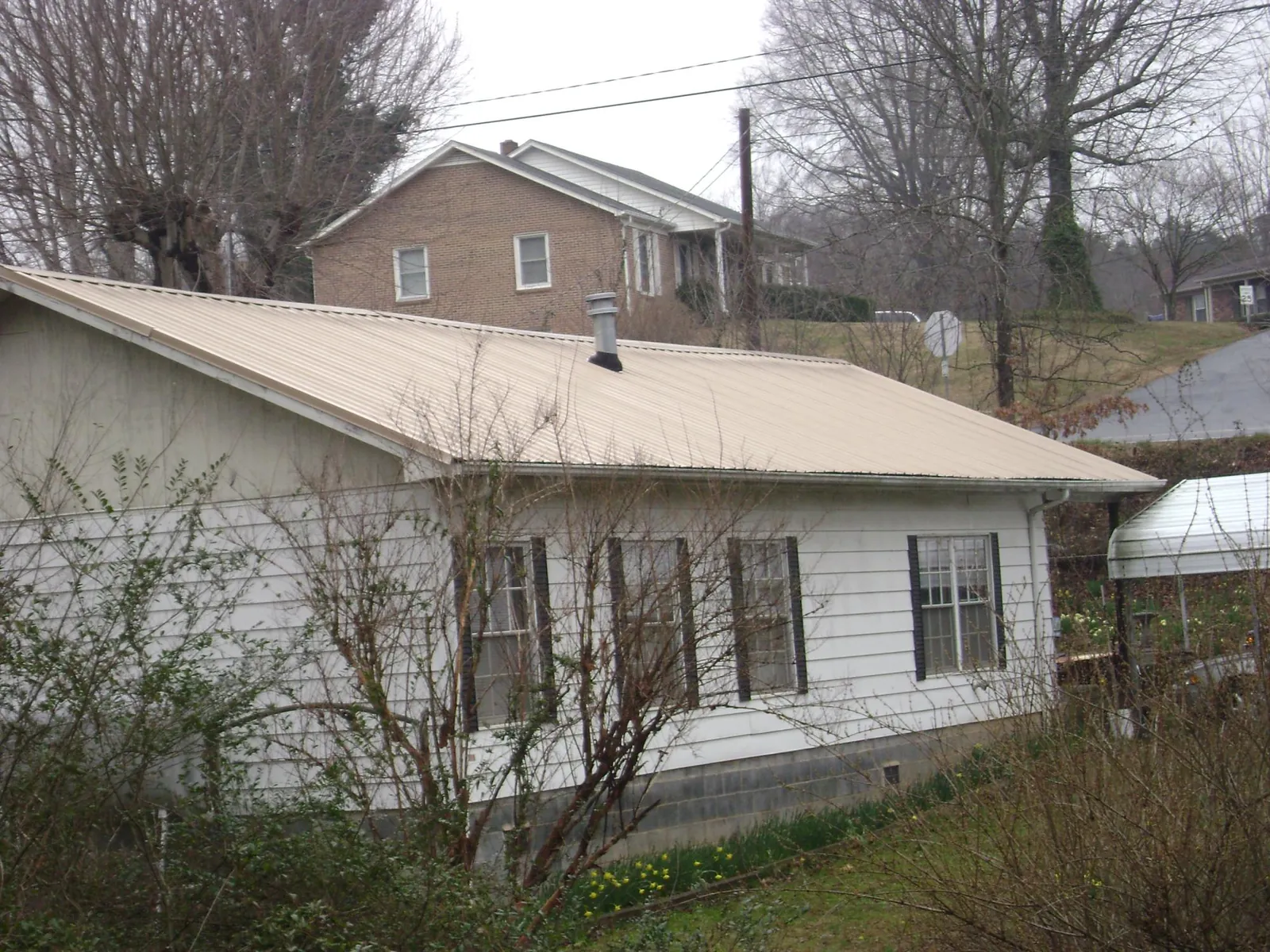 Tan metal roof on a white sided house set into a hillside — Commercial Roofing by Roofing Brothers in Osprey